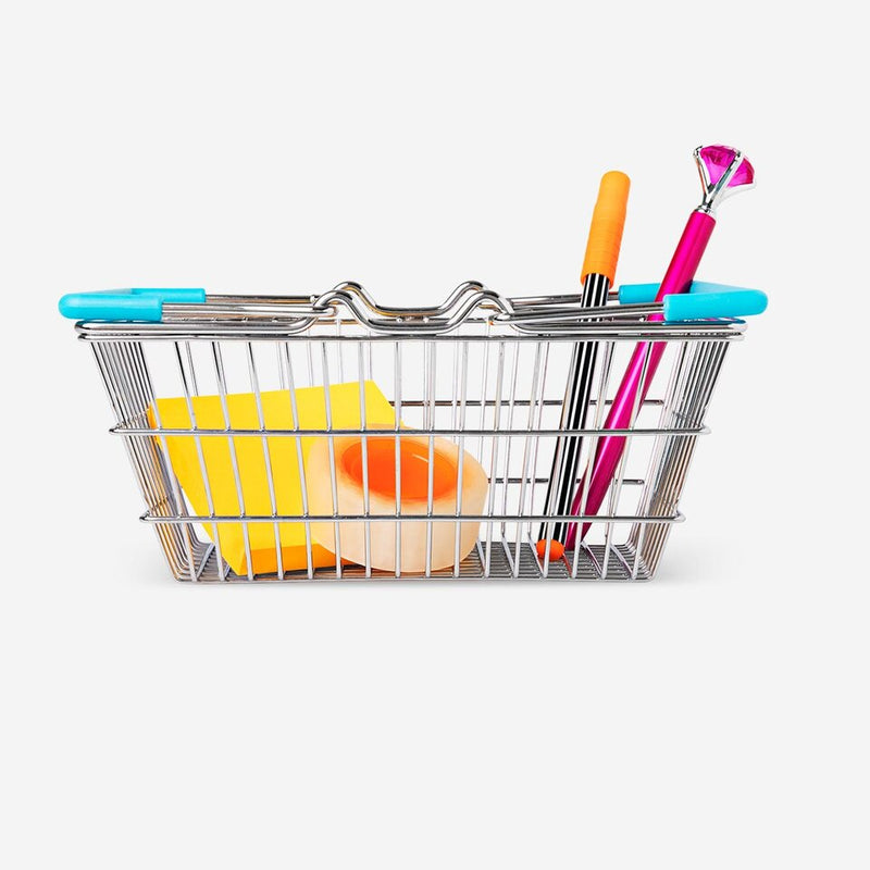 Miniature shopping basket filled with stationery items including sticky notes, tape, a striped pen, and a novelty pen with pink gem top.